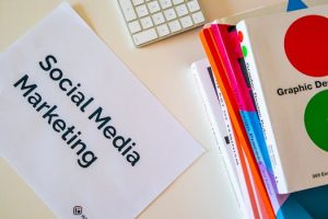 A top view of social media marketing text alongside graphic design books and a keyboard.